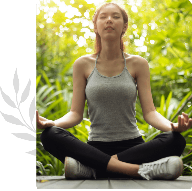Woman meditating outdoors in a peaceful green setting.