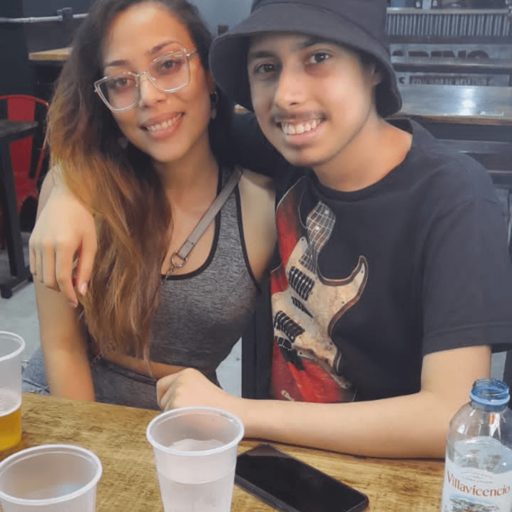 Two young people smiling at a casual gathering with drinks on the table.