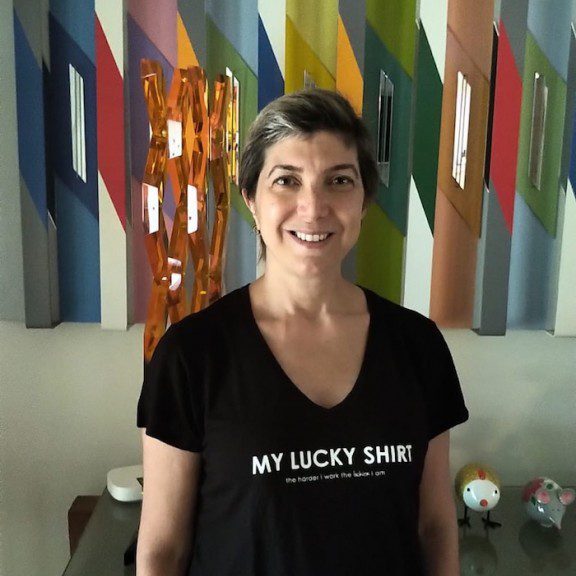 Smiling woman wearing a black 'My Lucky Shirt' tee in a colorful room.
