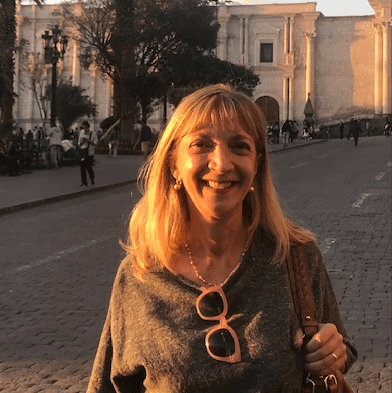 A smiling woman with blonde hair stands outdoors in the evening light.