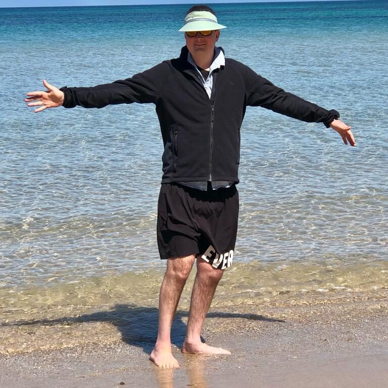 Person standing barefoot on the beach with arms outstretched.